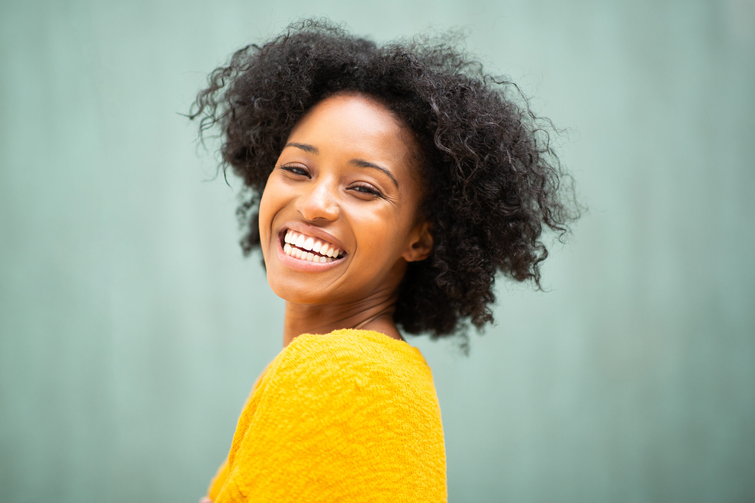 Close up portrait of smiling young black woman against green background looking at camera