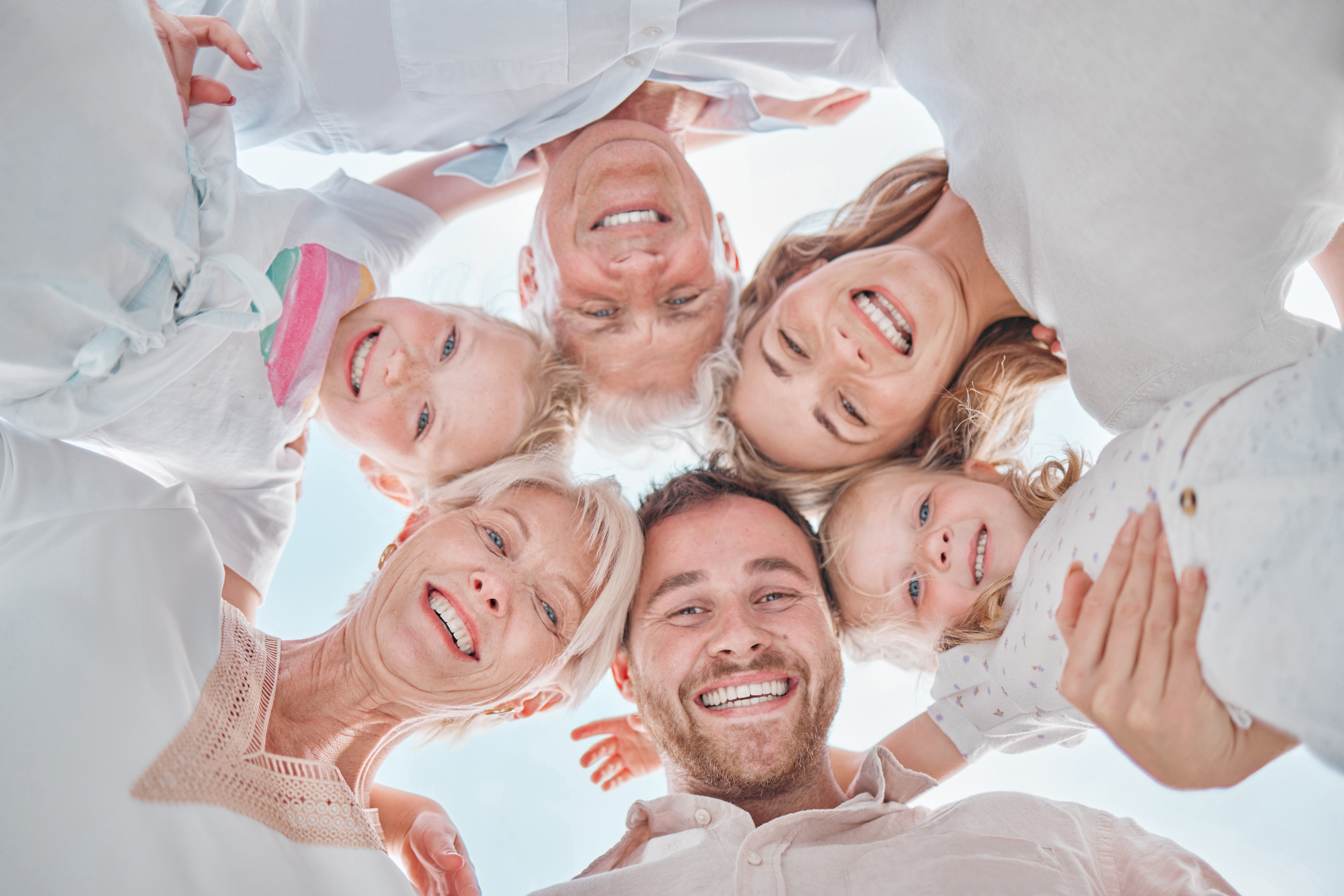 Happy cheerful caucasian family huddling together looking down while enjoying time in nature. Low angle of the faces of a carefree family hugging each other and relaxing outside on the weekend