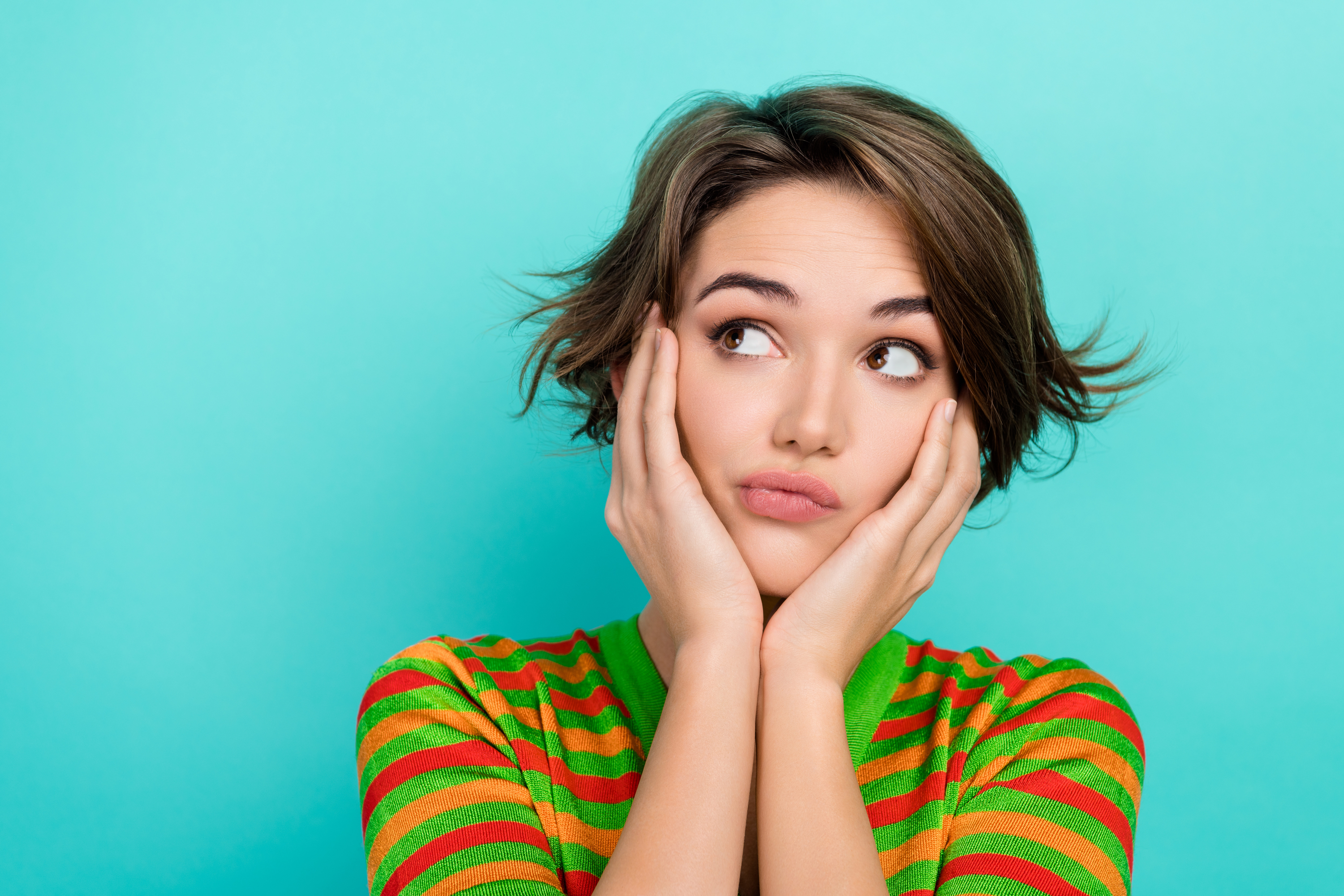 Photo of doubtful unsure woman dressed striped t-shirt arms cheeks looking empty space isolated turquoise color background.