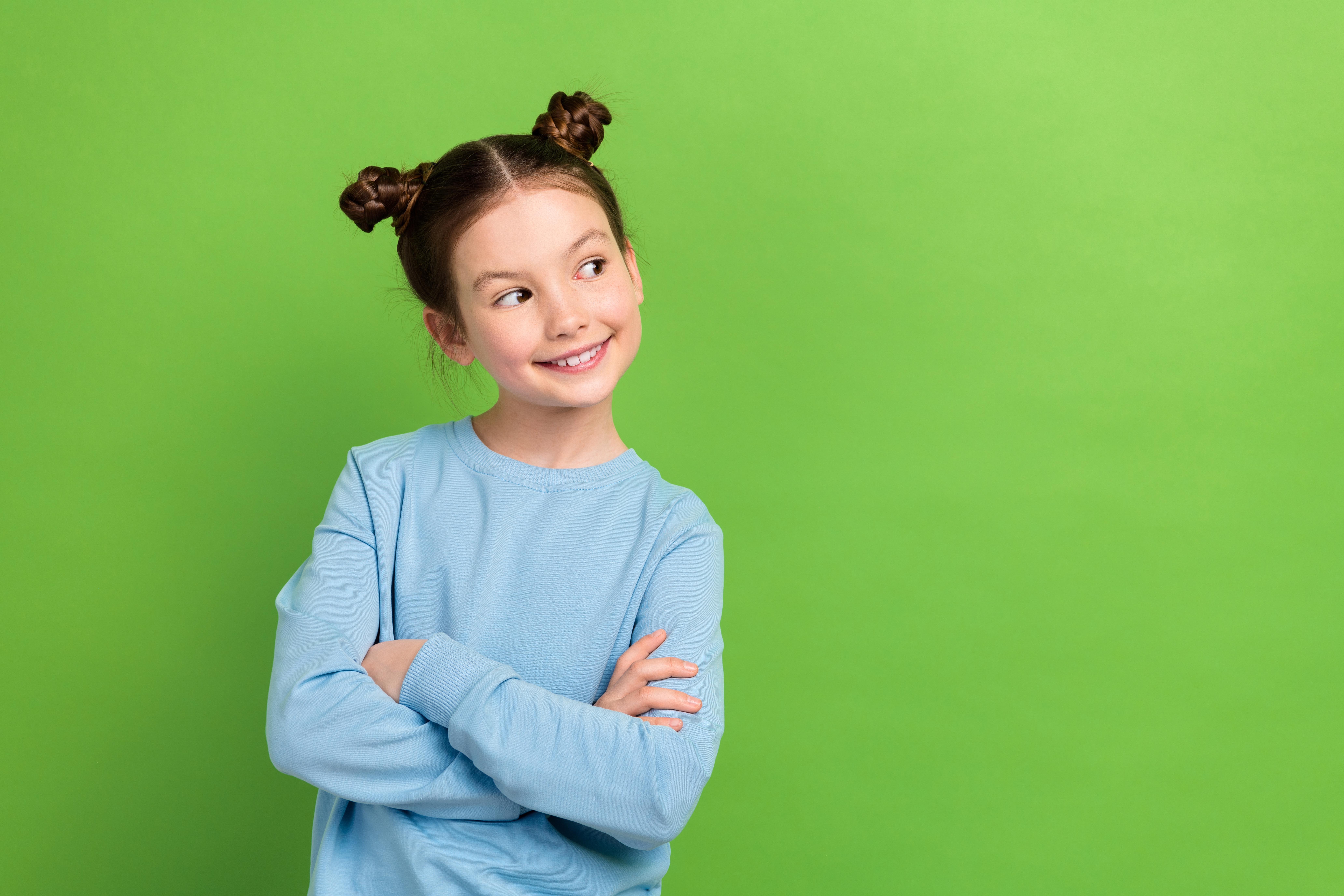 Portrait of adorable small girl with brown hair wear blue sweatshirt look empty space arms crossed isolated on green color background.